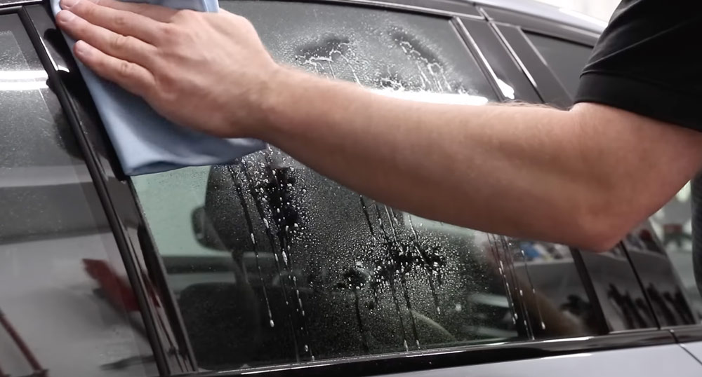homme nettoie les vitres de sa voiture avec un chiffon